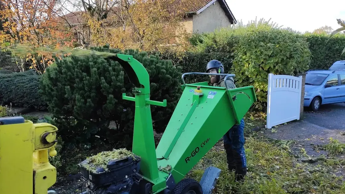 Broyeur de branches vert en fonctionnement devant une haie